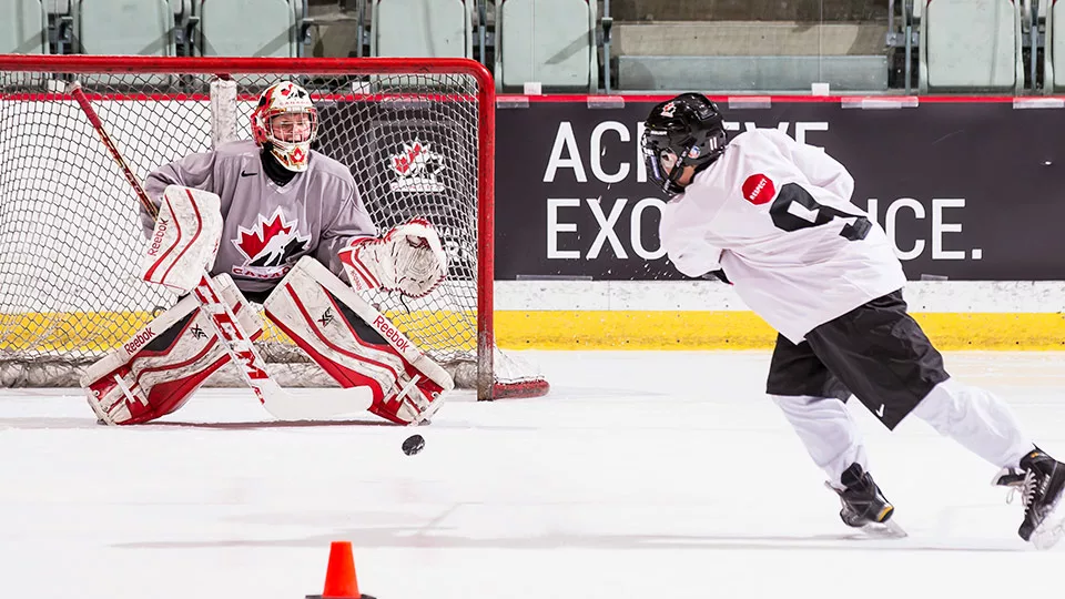 man taking aim for goal on hockey goalie